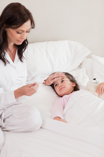 Stock photo: Portrait of a mother checking on her daughter's temperature in a bedroom