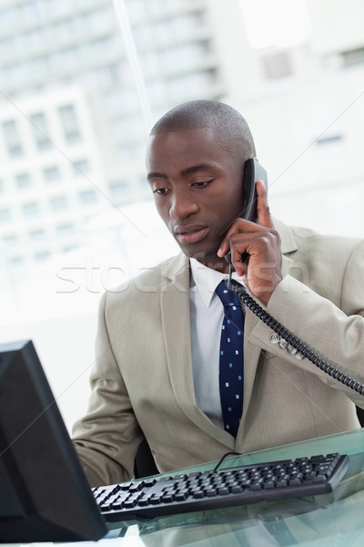 Stock photo: Portrait of an office worker making a phone call while using a computer