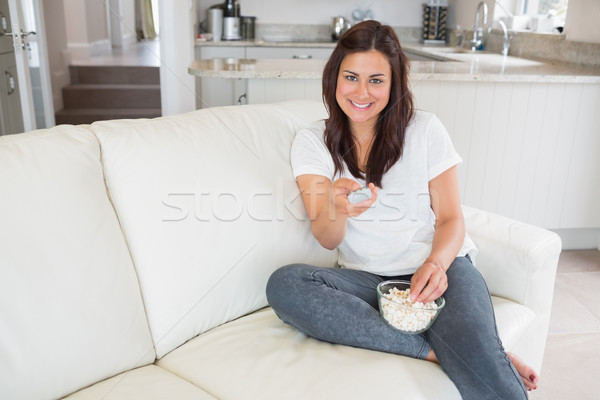 Brunette relaxing on the couch and smiling while eating popcorn with tv remote Stock photo © wavebreak_media