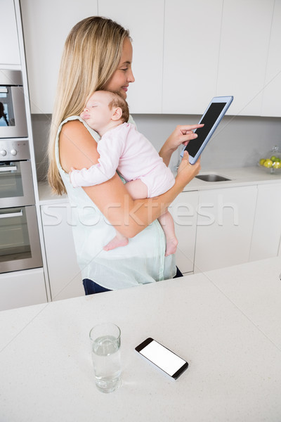 Mother using digital tablet while carrying her baby in kitchen Stock photo © wavebreak_media