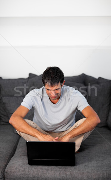 Radiant man using a laptop on a grey sofa Stock photo © wavebreak_media
