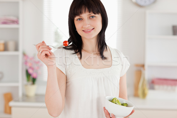 Attractive brunette female eating a cherry tomato while holding a bowl of vegetables in the kitchen Stock photo © wavebreak_media