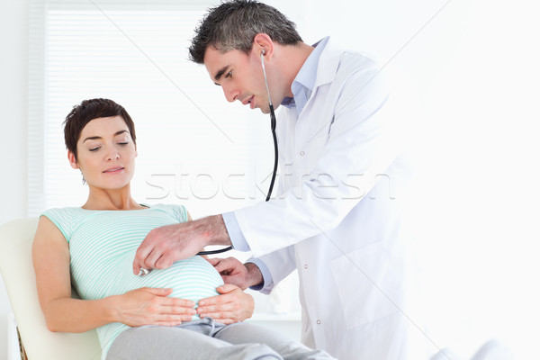 Doctor examining the cute woman's tummy with a stethoscope in a room Stock photo © wavebreak_media