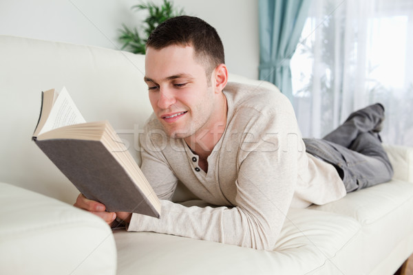 Young Man Lying On A Couch To Read A Book In His Living Room Stock