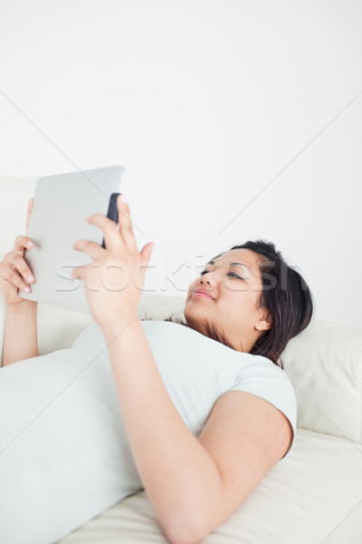 Woman lying on a sofa while holding a tactile tablet in a living room Stock photo © wavebreak_media