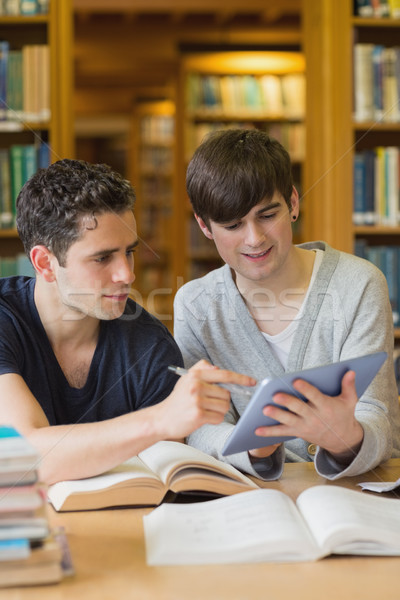 Stock photo: Smiling student showing another something on tablet pc studying in the library