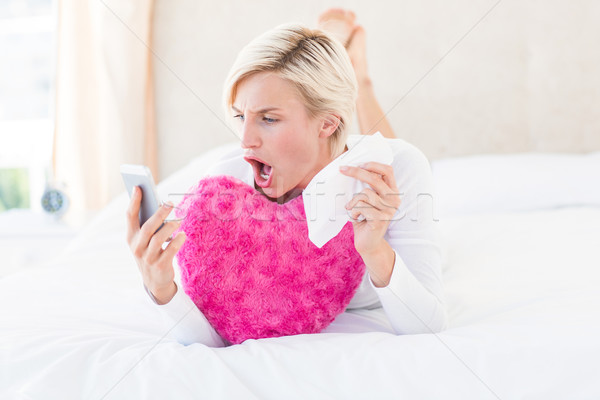 Shocked blonde woman lying on the bed and texting with her mobil Stock photo © wavebreak_media