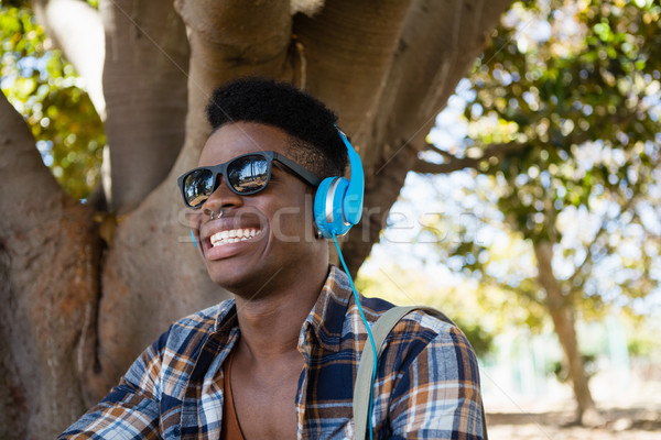 Foto stock: Moço · óculos · de · sol · fones · de · ouvido · ouvir · música · parque · árvore