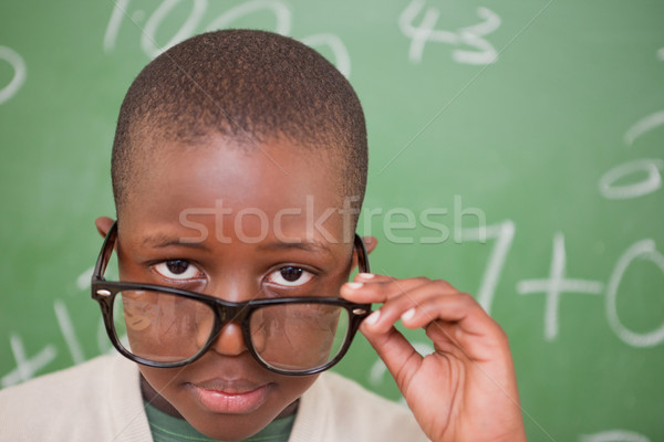Schoolboy looking over his glasses in front of a blackboard Stock photo © wavebreak_media