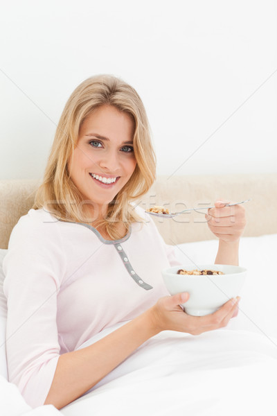 A woman sitting in bed with a bowl of cereal in hand and a spoon of cereal near her mouth, while loo Stock photo © wavebreak_media