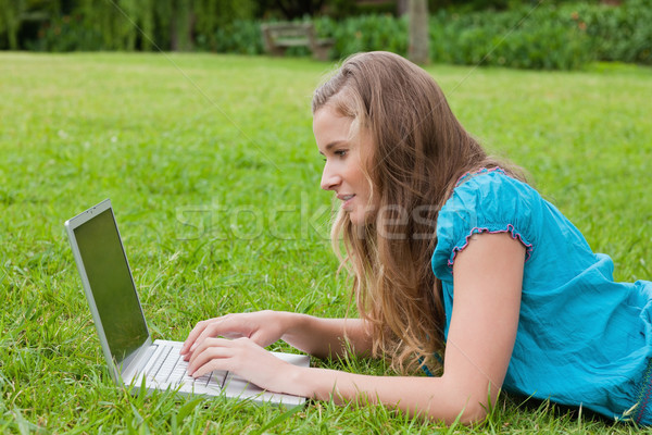 Side view of a young girl typing on her laptop while lying down in the countryside Stock photo © wavebreak_media