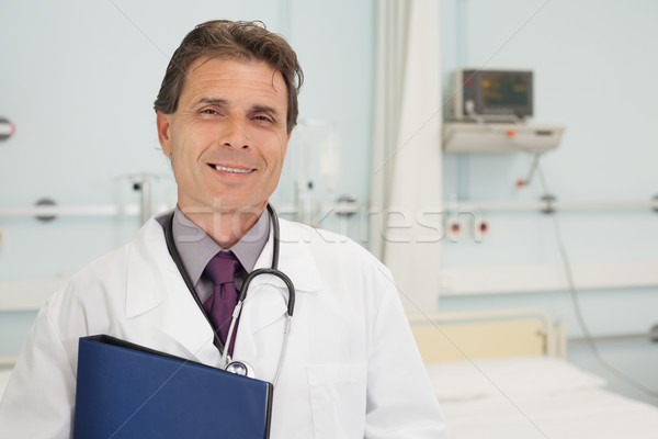 Stock photo: Smiling doctor holding a folder in hospital bedroom