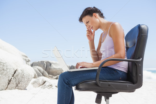 Pretty brunette using laptop on the beach sitting on swivel chai Stock photo © wavebreak_media