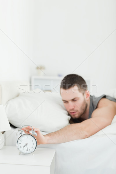 Stock photo: Portrait of a tired man being awakened by an alarm clock in his bedroom