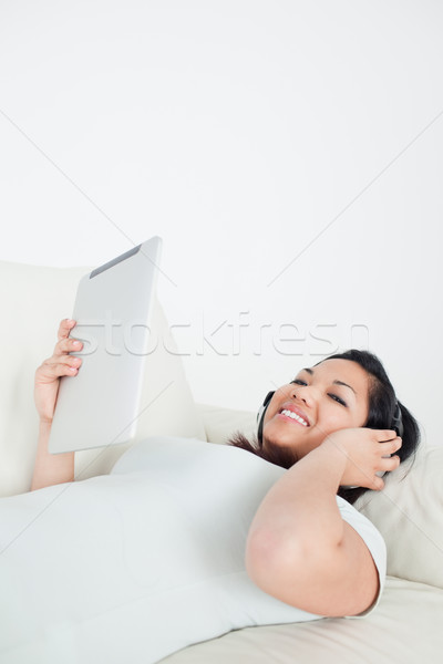 Woman lies on a sofa with headphones on and holding a tactile tablet in a living room Stock photo © wavebreak_media