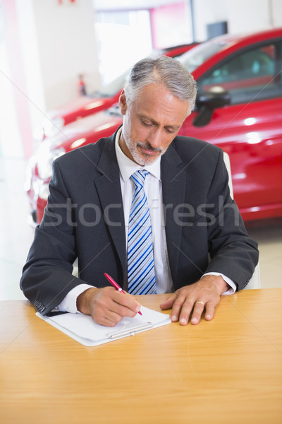 Focused salesman writing on clipboard at his desk Stock photo © wavebreak_media