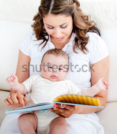 Attentive mother reading a book to her adorable baby sitting in the couch in the living-room Stock photo © wavebreak_media