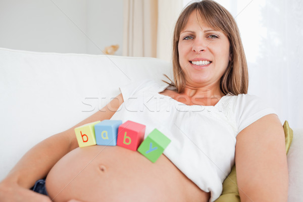 Lovely pregnant female playing with wooden blocks while lying on a sofa in her living room Stock photo © wavebreak_media