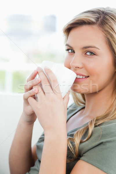 A close up shot of a smiling woman looking in front of her with a cup to her lips. Stock photo © wavebreak_media