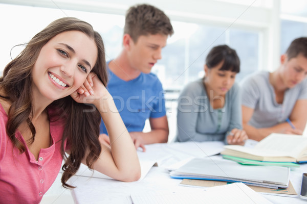A girl sits beside her studying friends as she looks into the camera and rests her head upon her han Stock photo © wavebreak_media