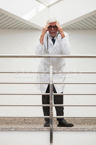 Stock photo: Stressed doctor is leaning on the railing with hands on his forehead while in hospital corridor