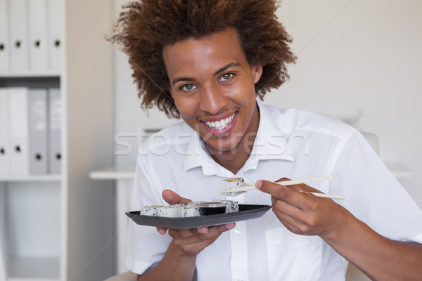Casual smiling businessman eating sushi at his desk Stock photo © wavebreak_media
