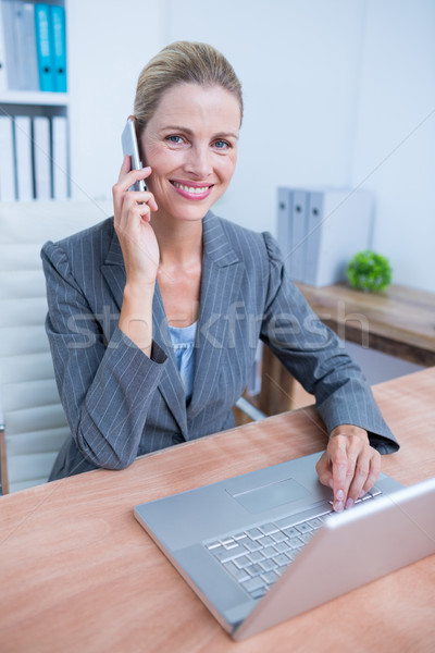 Pretty blonde businesswoman phoning and using her laptop Stock photo © wavebreak_media