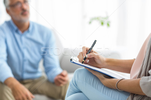 Stock photo: Female doctor writing on clipboard while consulting a man