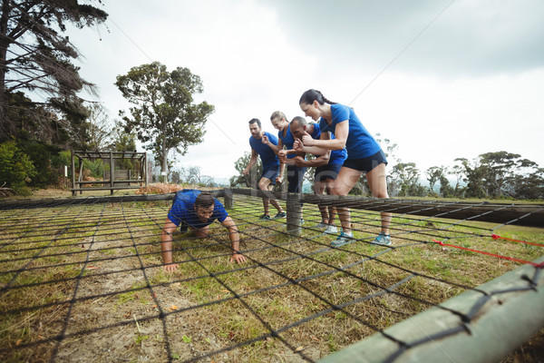 Fit man crawling under the net during obstacle course while fit people cheering Stock photo © wavebreak_media