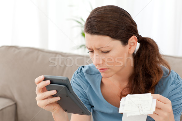 Attractive woman holding a calculator and bills while doing her accounts at home Stock photo © wavebreak_media