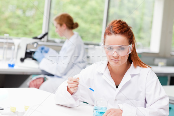 Science student dropping blue liquid in a beaker while looking at the camera Stock photo © wavebreak_media
