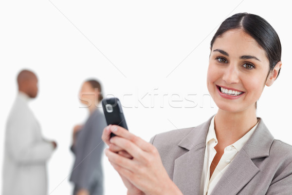 Smiling saleswoman holding cellphone with colleagues behind her against a white background Stock photo © wavebreak_media