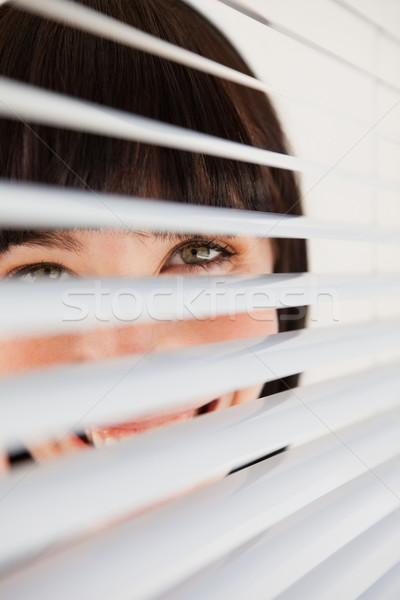 A woman smiling as she glances into the camera through some blinds Stock photo © wavebreak_media