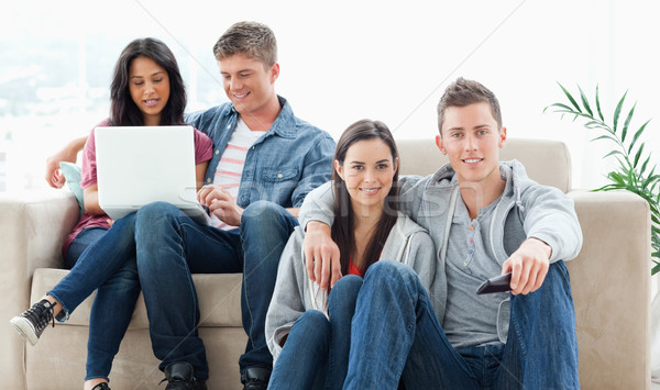 A smiling couple on the ground with a tv remote while another group sit on the couch together with a Stock photo © wavebreak_media
