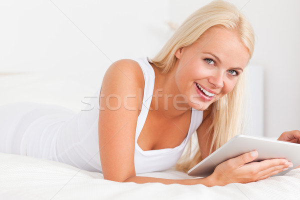 Stock photo: Smiling woman with a tablet computer while lying on her bed