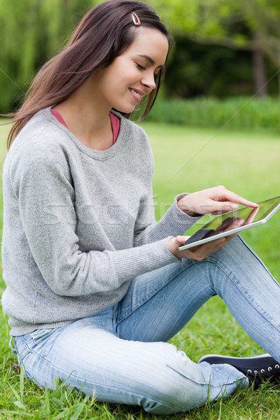Stock photo: Young woman sitting on the grass in a parkland while holding a tablet computer