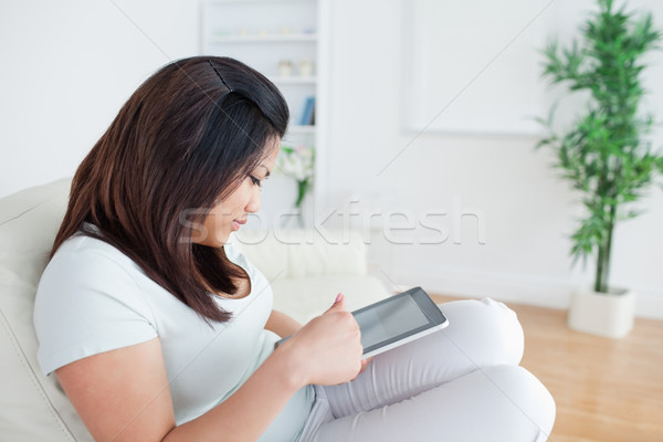 Woman sitting on a sofa while holding and playing with a tactile tablet in a living room Stock photo © wavebreak_media