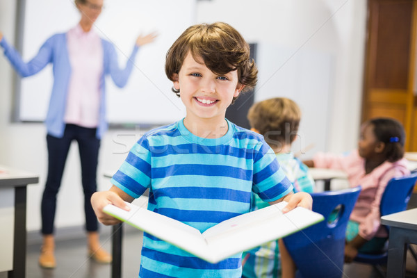Portrait of schoolboy standing with book in classroom Stock photo © wavebreak_media