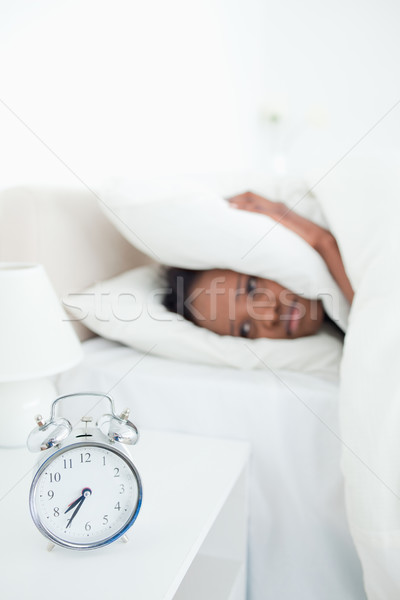 Portrait of a tired woman covering her ears while her alarm clock is ringing in her bedroom Stock photo © wavebreak_media