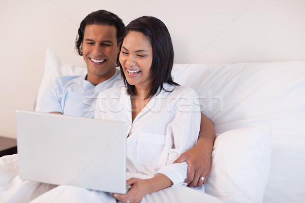 Stock photo: Young couple using their laptop while sitting on the bed
