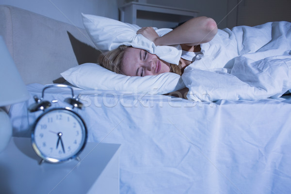Woman covering ears with pillow as alarm clock rings Stock photo © wavebreak_media