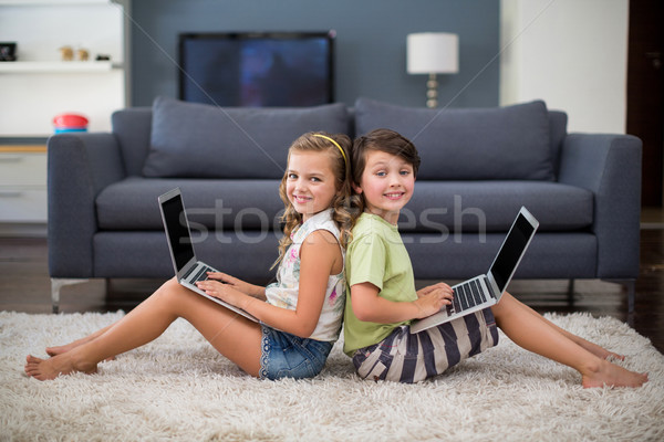 Smiling siblings sitting back to back and using laptop in living room Stock photo © wavebreak_media