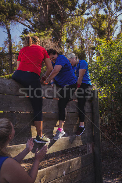 Stock photo: Woman being assisted by her teammates to climb a wooden wall during obstacle course training