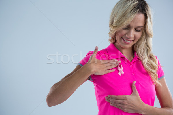 Smiling woman with pink ribbon touching on breast Stock photo © wavebreak_media