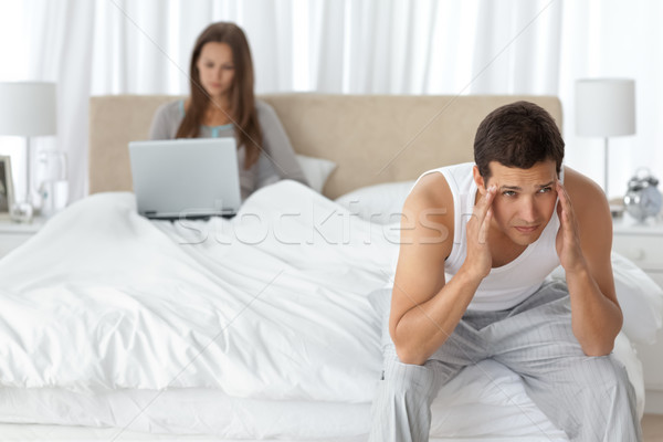 Man having a headache in the bedroom with his girlfriend working on the background Stock photo © wavebreak_media