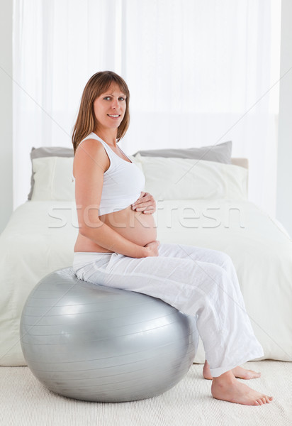Stock photo: Attractive pregnant female caressing her belly while sitting on a gym ball in her bedroom