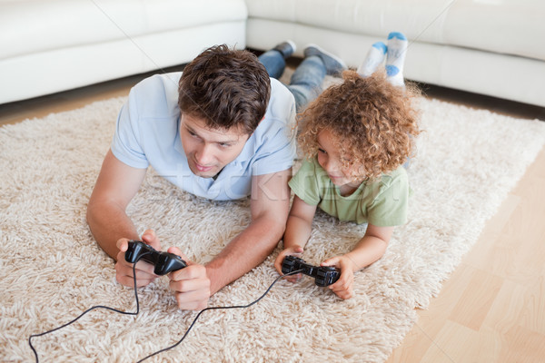 Stock photo: Focused boy and his father playing video games while lying on a carpet