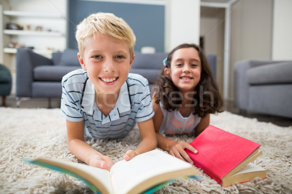 Portrait of siblings lying on rug and reading book in living room Stock photo © wavebreak_media