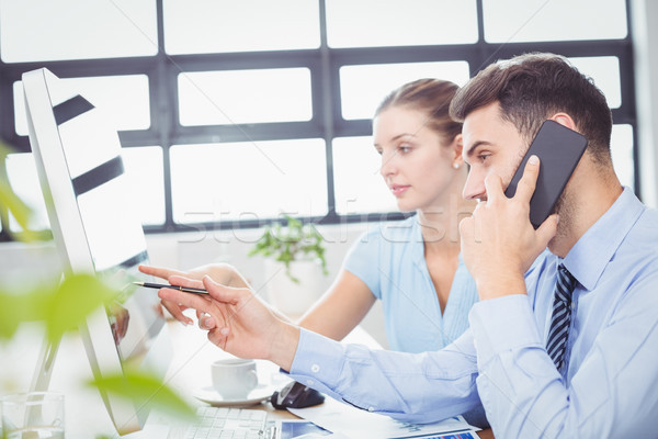 Businessman talking on mobile phone while pointing at computer m Stock photo © wavebreak_media