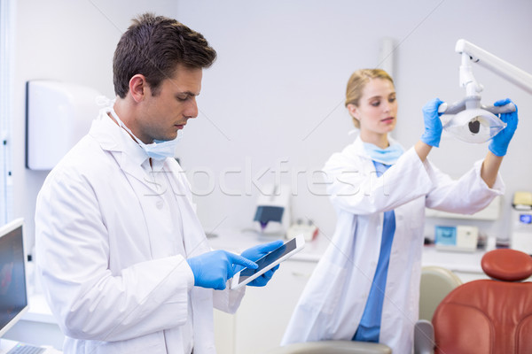 Stock photo: Dentist using digital tablet while his colleague adjusting dental light in background